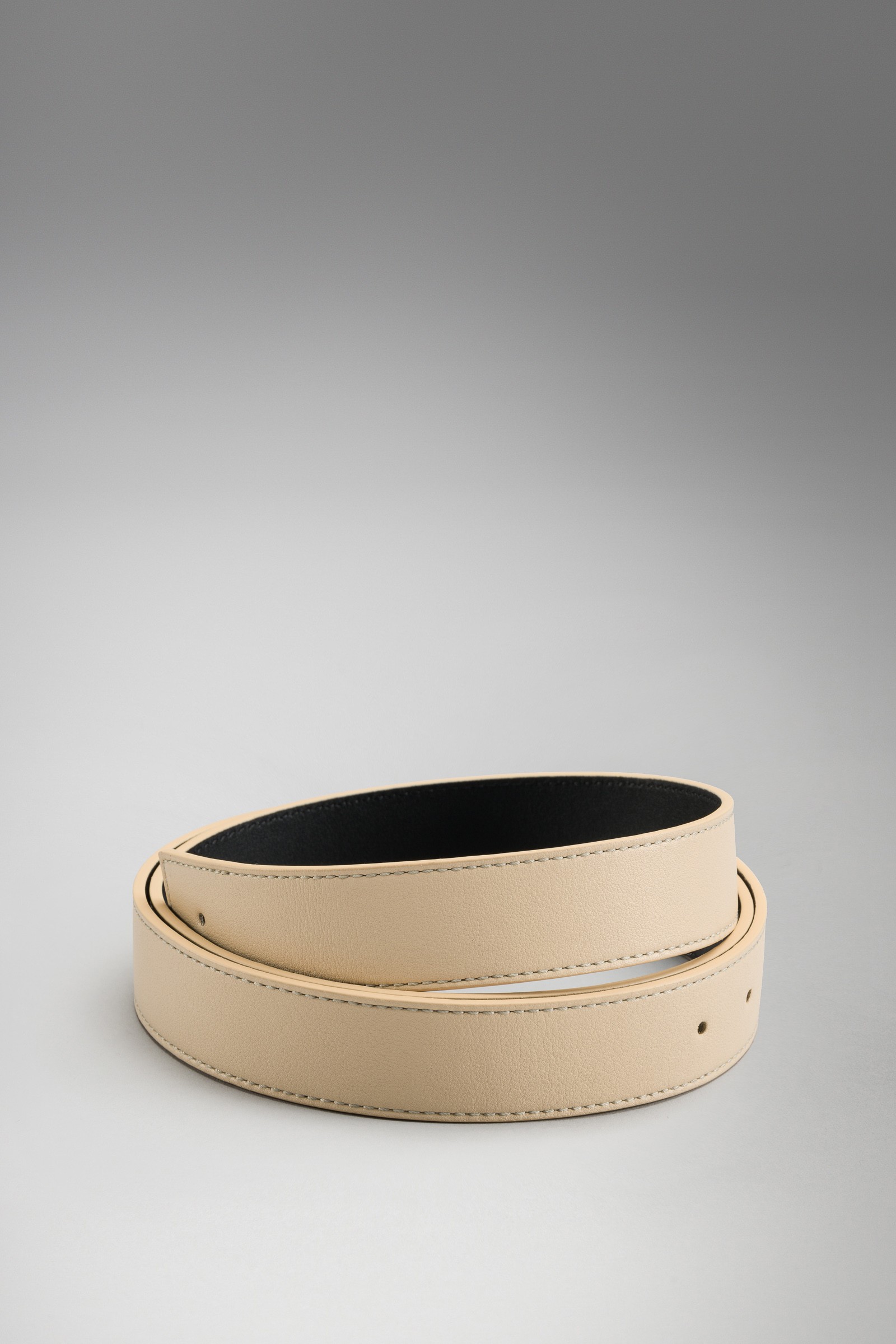 Beige tan leather belt coiled on a plain gray background, smooth finish, minimalist product shot